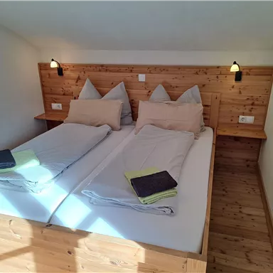 Ein gemütliches Zimmer mit zwei Einzelbetten und Holzverkleidung. Die Bettwäsche ist ordentlich und es sind kleine Handtücher auf den Betten platziert.