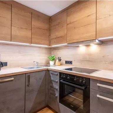 Eine moderne Küche mit Holzoberflächen und Edelstahlgeräten. Es gibt einen Wasserkocher, einen Herd und eine Flasche Wein auf der Arbeitsplatte.