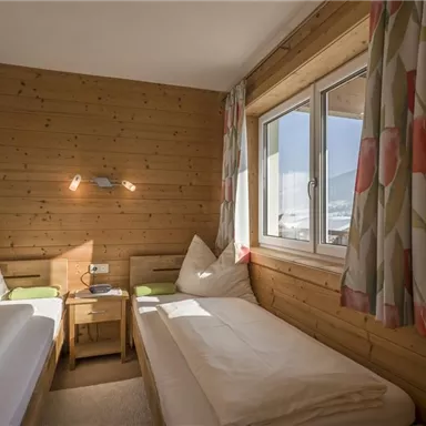 A cozy room with two single beds and wood paneling. The window lets in plenty of daylight and offers a view of the surroundings.