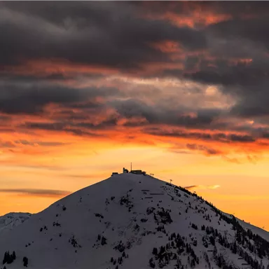 A snow-covered mountain under an orange sunset. The clouds are dramatic and give the scene a mystical atmosphere.