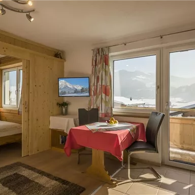 A cozy holiday apartment with wooden details and large windows. The view of the mountains and the bright decor create an inviting atmosphere.