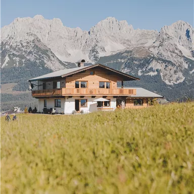 A beautiful house in the mountains, surrounded by green meadows. In the background, majestic mountains are visible.