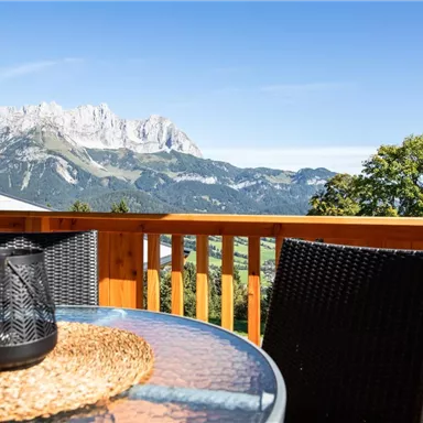 A beautiful balcony with a view of majestic mountains and a clear sky landscape. A table with a decorative placemat and a candle holder invites you to relax.