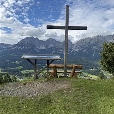 A view of the mountains with a wooden cross in the foreground. A bench-table combination invites you to linger.