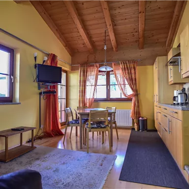 Eine gemütliche Wohnung mit Holzdetails und gelben Wänden. Sie verfügt über eine Küche, einen Essbereich und große Fenster mit roten Vorhängen.