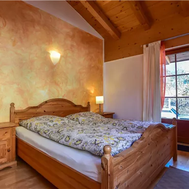 Ein gemütliches Schlafzimmer mit einem Holzbett und bunten Wänden. Neben dem Bett stehen zwei Nachttische mit Lampen und eine große Tür führt nach draußen.