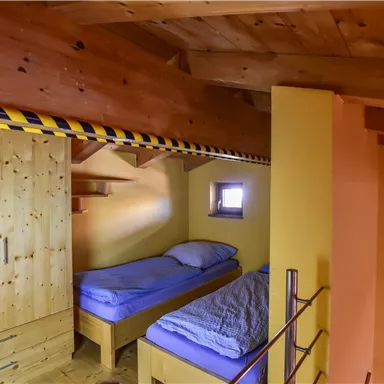 Ein gemütliches Schlafzimmer mit zwei Einzelbetten und Holzschränken. Die Wände sind in warmen Farben gehalten, und es gibt ein kleines Fenster.