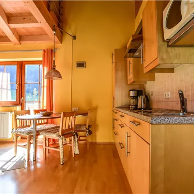 Eine helle Küchenzeile mit Holzmöbeln, einem Tisch und Stühlen. Die Fenster lassen viel Tageslicht herein und schaffen eine gemütliche Atmosphäre.