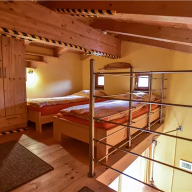 Ein gemütliches Zimmer mit Holzverkleidung und zwei Betten. Die Fassade ist hellgelb, und es gibt einen modernen Geländer im Obergeschoss.