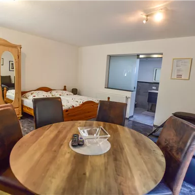 Ein gemütliches Zimmer mit einem runden Esstisch und Stühlen. Im Hintergrund sind ein Bett und ein Spiegel-Schrank sichtbar.