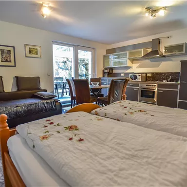 Ein gemütliches Zimmer mit zwei Betten und einer modernen Küchenzeile. Große Fenster sorgen für viel natürliches Licht und einen Blick ins Freie.