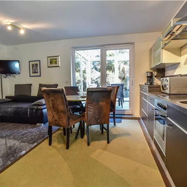 Eine moderne Küche mit einem Essbereich und einem Wohnzimmer. Große Fenster bieten Blick auf den Garten.