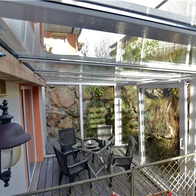 Ein gemütlicher Wintergarten mit einem Tisch und Stühlen. Große Fenster bieten Blick auf die Natur draußen.