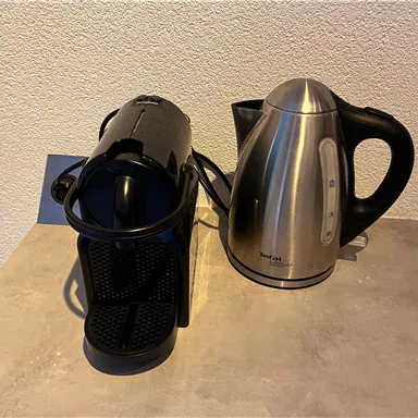 Ein schwarzer Kaffeeautomat und ein silberner Wasserkocher stehen nebeneinander auf einer grauen Arbeitsfläche. Beide Geräte sind modern und praktisch für die Küche.