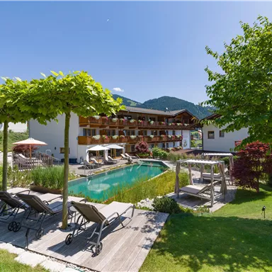 Exterior view of Hotel Alpenpanorama with garden, pool, sun loungers, and view of the Tyrolean mountains.
