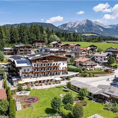Außenansicht des Hotels Alpenpanorama in Söll mit Garten, Terrasse und Blick auf die Tiroler Bergwelt.