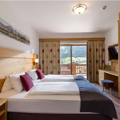 Double room at Hotel Alpenpanorama in the Wilder Kaiser holiday region with wooden furniture, cozy sitting area, and a view of nature.