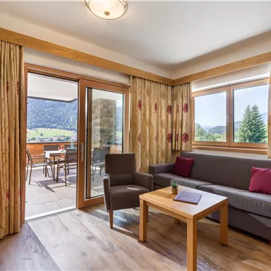 A cozy living space with a sofa, a table, and a TV. Large windows offer a view of nature and a terrace.