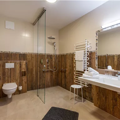 A modern bathroom with wooden paneling and a large shower. There is a sink, a mirror, and a towel holder.
