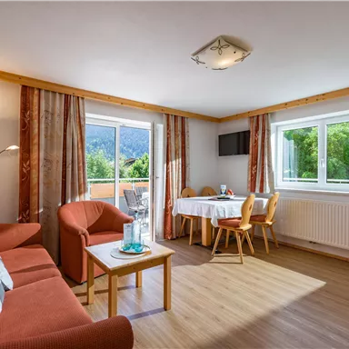 A cozy living room with a red sofa and a table. Large windows provide a view of the green landscape.