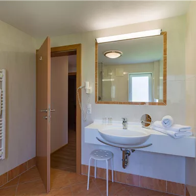 A modern bathroom with a sink and a large mirror. The walls are bright and there is access to another room.