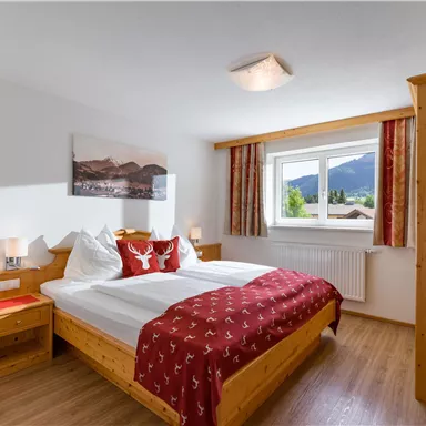 A cozy bedroom with a double bed and wooden furniture. The window offers a view of the mountains and provides plenty of daylight.