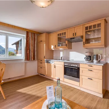 A bright kitchen with wooden cabinets and modern appliances. It offers a view of the mountains through a large window.