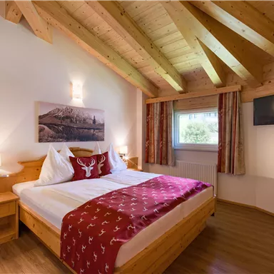 A cozy bedroom with wooden details and a large bed. The room has light walls and a window with a view outside.