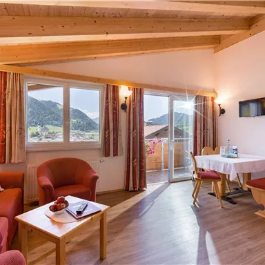 A bright and inviting living room with a wooden ceiling and modern furniture. Large windows provide a magnificent view of the mountains.