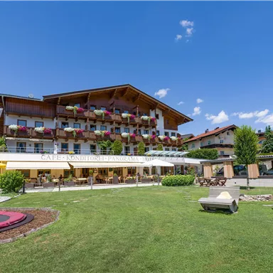 A beautiful hotel with rich floral decorations and a large garden. In the background, clear blue skies and trees can be seen.
