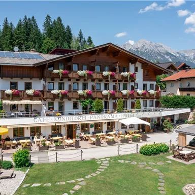 A charming guesthouse in a picturesque landscape with colorful flower boxes. The terrace invites you to relax outdoors, surrounded by green meadows and mountains in the background.