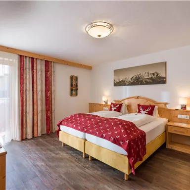 A cozy bedroom with a double bed and wood-colored furnishings. Large windows provide ample daylight.