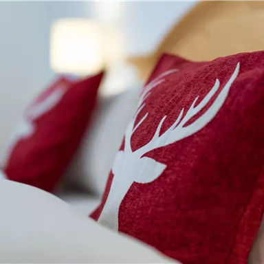 Decorative cushions with deer motif on a bed. The background shows a soft, bright atmosphere.