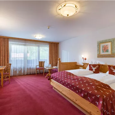 Comfort room at Hotel Alpenpanorama in the Wilder Kaiser holiday region with box spring bed, red carpet, and balcony access.