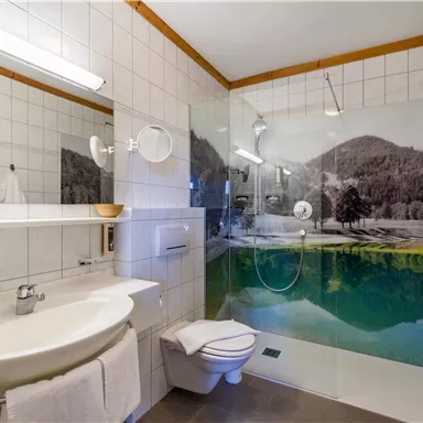 Modern bathroom at Hotel Alpenpanorama in the Wilder Kaiser holiday region with shower, large mirror, and alpine wall motif.