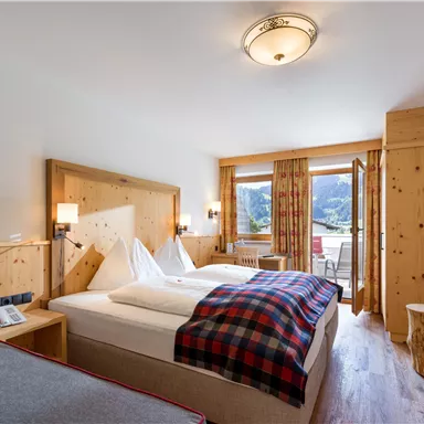 Cozy double room at Hotel Alpenpanorama in the Wilder Kaiser holiday region with wooden bed, checkered blanket, and mountain view.