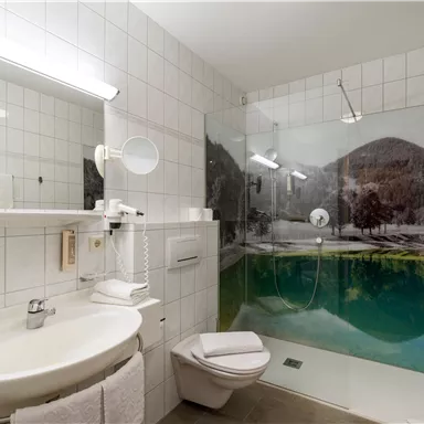 A modern bathroom with a glass shower and an elegant sink. The walls are brightly tiled and showcase a picturesque landscape in the background.