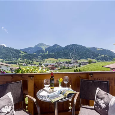 A cozy balcony with a view of the mountains and the valley. Drinks and a magazine are on the table.
