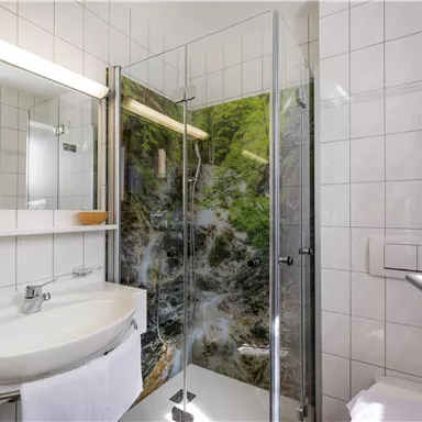 A modern bathroom with a shower cabin and a sink. The walls are brightly tiled and a green landscape is depicted as shower panels.