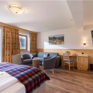 A cozy hotel room with wooden decor. There is a double bed, a seating area, a table, and a television.