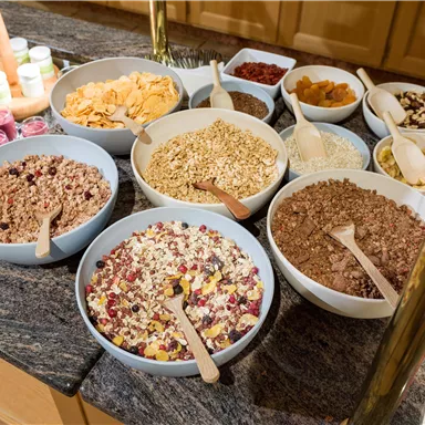 A selection of cereals in bowls on a table. There are different varieties and toppings that can be served for breakfast.