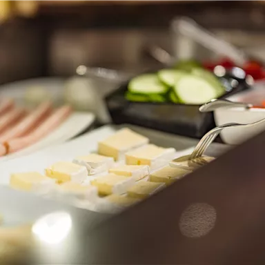 A buffet with various types of cheese, cold cuts, and sliced cucumbers. The colors are fresh and inviting.