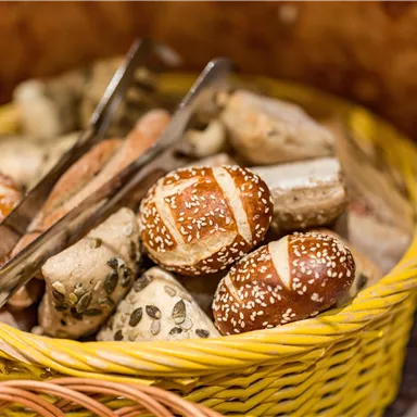 A basket with various rolls, including pretzels and multigrain varieties. The rolls are fresh and appetizingly arranged.