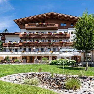 Ein charmantes Gasthaus in einer malerischen Landschaft mit bunten Blumenkästen. Die Terrasse lädt zum Entspannen im Freien ein, umgeben von grünen Wiesen und Bergen im Hintergrund.