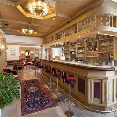 An elegant bar with wooden paneling and cozy seating. The area is brightly lit and decorated with a variety of drinks.