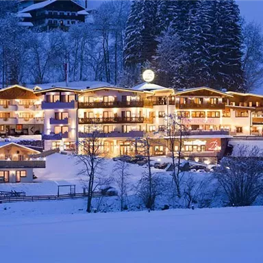 A cozy hotel that glows in the snow at night. Surrounded by snow-covered trees and a wintry landscape.