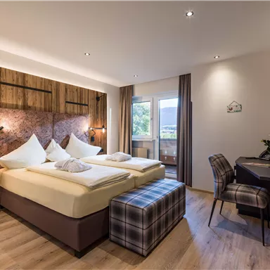 Ein modernes Hotelzimmer mit zwei Einzelbetten und Holzdekor. Es gibt einen Schreibtisch, eine gemütliche Sitzgelegenheit und einen Balkon mit Blick nach draußen.