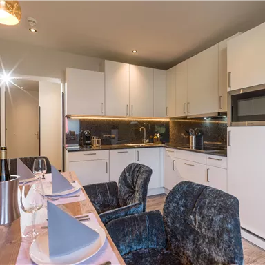 Moderne Küche mit weißen Schränken und schwarzer Arbeitsplatte. Ein Essbereich mit eleganten Stühlen und Tischdekoration ist ebenfalls sichtbar.