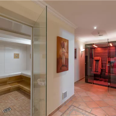 Ein moderner Spa-Bereich mit einer Sauna auf der linken Seite und einer Infrarotkabine auf der rechten Seite. Die Wände sind hell und die Bodenfliesen sind aus Stein.