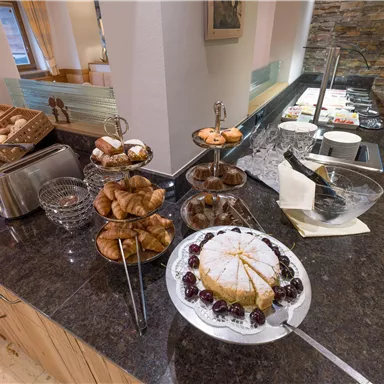 Ein reichhaltiges Frühstücksbuffet mit verschiedenen Backwaren und einer Torte auf einem eleganten Tisch. Frische Croissants und Kekse sind ebenfalls bereit zum Genießen.
